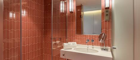 A modern bathroom with a glass-enclosed shower, a white sink with a mirror, and a red patterned wall.