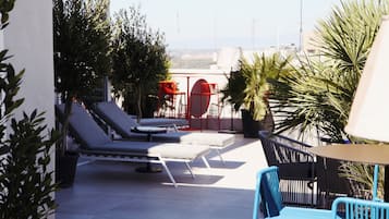 A rooftop terrace with lounge chairs, a table, and potted plants.