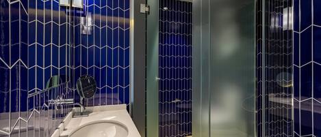 A modern bathroom with a glass shower enclosure, a white sink, and a blue patterned wall.