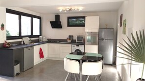 A compact kitchen with a built-in oven, microwave, and refrigerator. There is a small dining area with two chairs and a glass table. - Seasonal rental brand new - 4 pers. -POSSESSION-end construction Oct. 19 (LA POSSESSION)