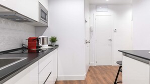 A modern kitchen with white cabinets, a black countertop, a red coffee machine, and a small potted plant.