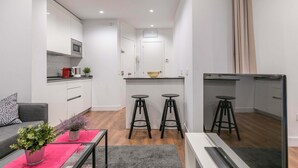 A compact apartment with a kitchenette, a dining area with stools, a sofa, and a coffee table with a plant.