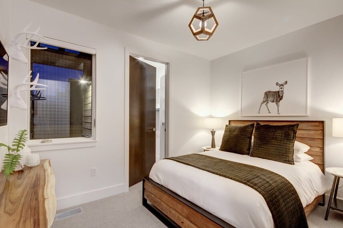 Une chambre avec un lit en bois, une fenêtre donnant sur un beau paysage, une décoration murale représentant un cerf et une table de chevet avec une lampe.