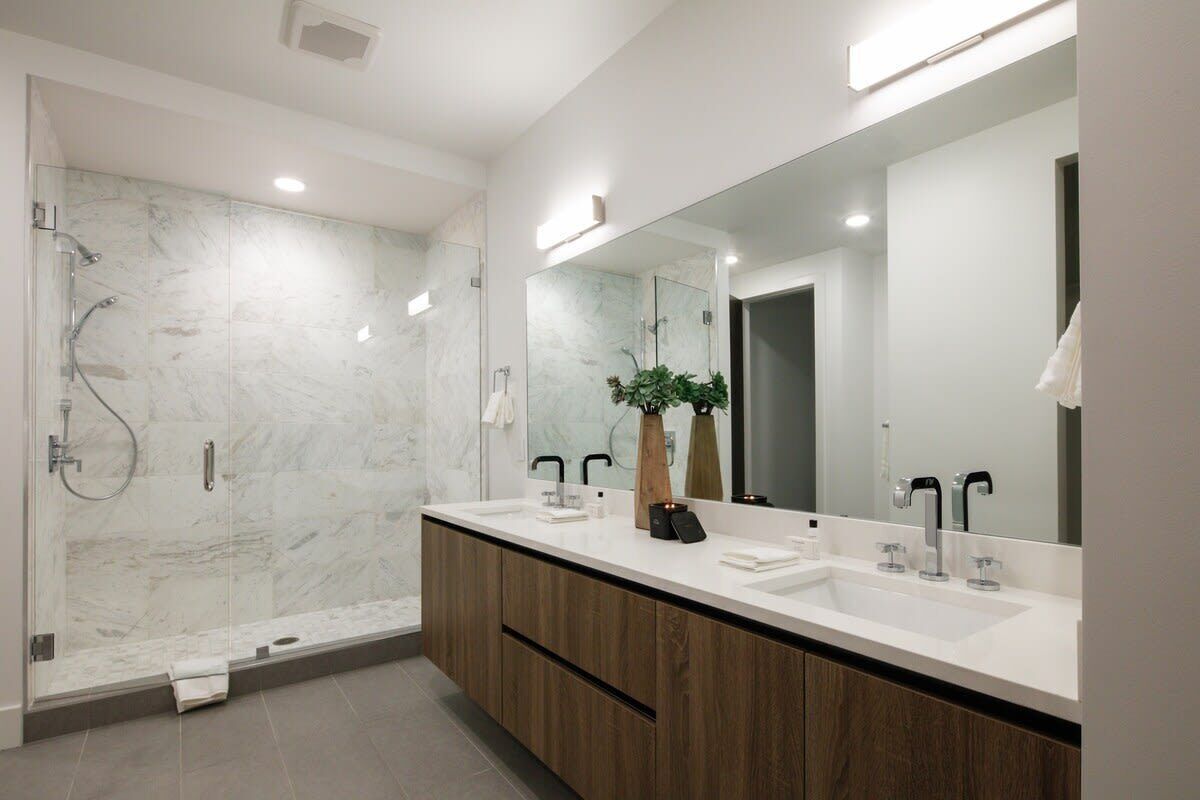 A modern bathroom with a glass-enclosed shower, a large mirror, and wooden cabinets.