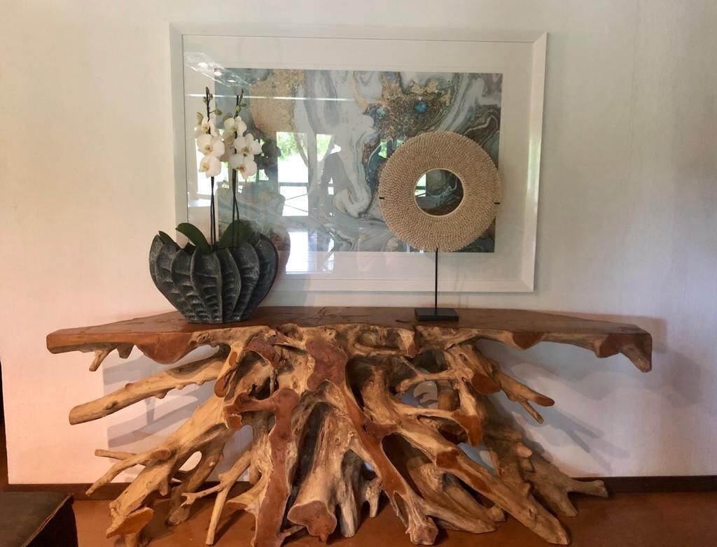 Eine Holzskulptur mit baumähnlichem Design auf einem Tisch, ein gerahmtes abstraktes Gemälde und ein gewebter Korb auf einem Ständer.