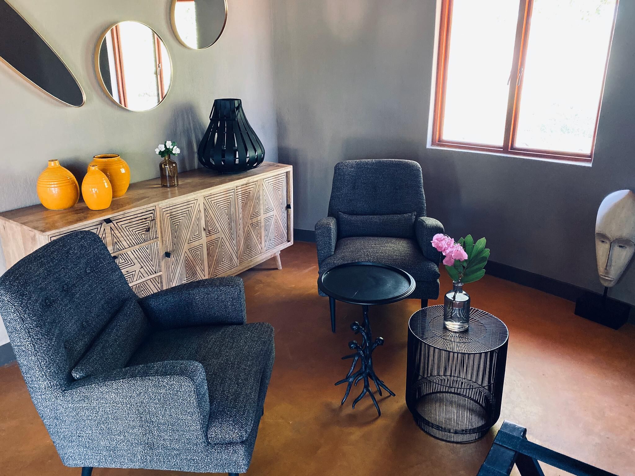 A modern living room with a grey armchair, a wooden cabinet with geometric patterns, and a round black table.