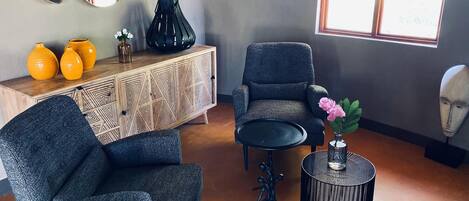 A modern living room with a grey armchair, a wooden cabinet with geometric patterns, and a round black table.
