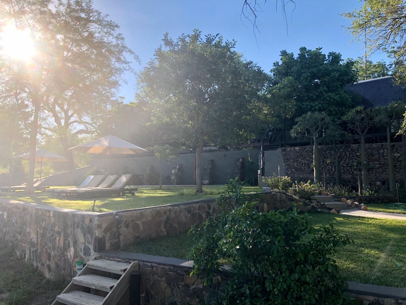 A backyard with a stone wall, a wooden deck, and a grassy area.