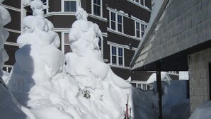 Uma trilha coberta de neve conduz a um edifício com entrada lateral e um bastão de esqui à vista.