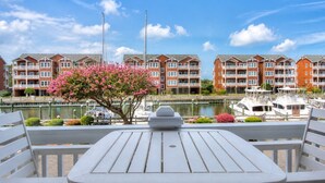 Vista al agua con una mesa y sillas, un árbol floreciente de color rosa y una hilera de edificios de ladrillo rojo.
