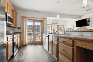 Una cocina con armarios de madera, un refrigerador de acero inoxidable, horno empotrado, una isla grande con un lavamanos y vistas al exterior a través de la puerta de vidrio.