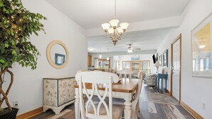 Un comedor con candelabro, una mesa de madera, sillas blancas y una planta en maceta.