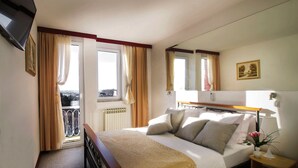 A hotel room with a bed, bedside table, lamp, and a view of the outside. - Hotel Slavonija (Vinkovci)