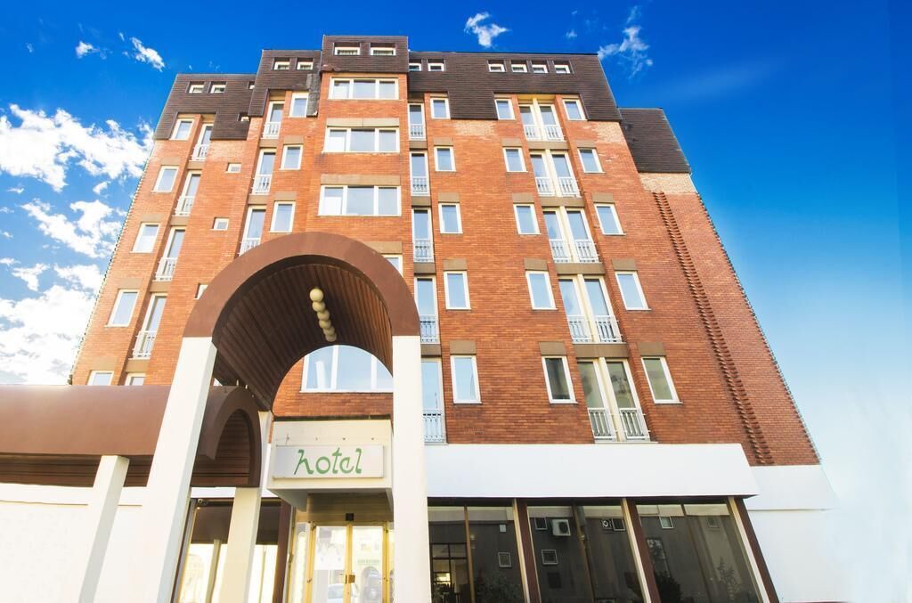 Un hotel de varios pisos con fachada de ladrillo, amplias ventanas y un arco pronunciado en la entrada.