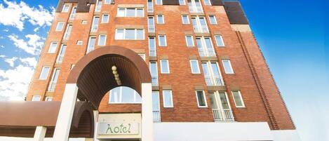 Un hotel de varios pisos con fachada de ladrillo, amplias ventanas y un arco pronunciado en la entrada.
