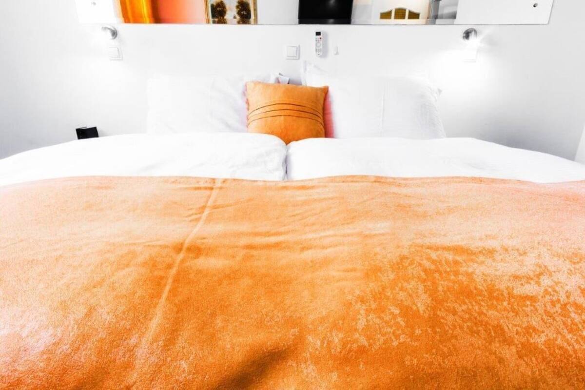 A bed with an orange blanket and white pillows.