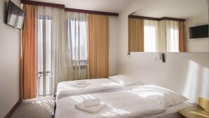 A hotel room with two beds, a TV, a mirror, and a window with curtains. - Hotel Slavonija (Vinkovci)