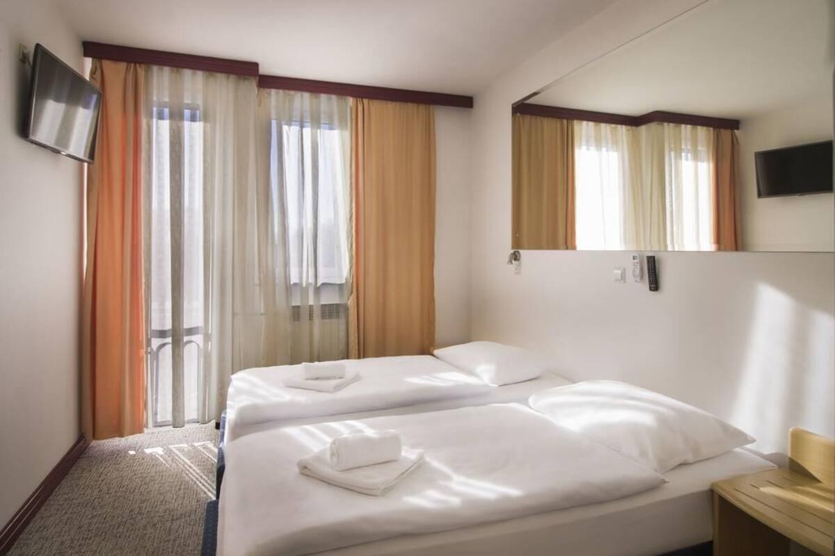 A hotel room with two beds, a TV, a mirror, and a window with curtains.