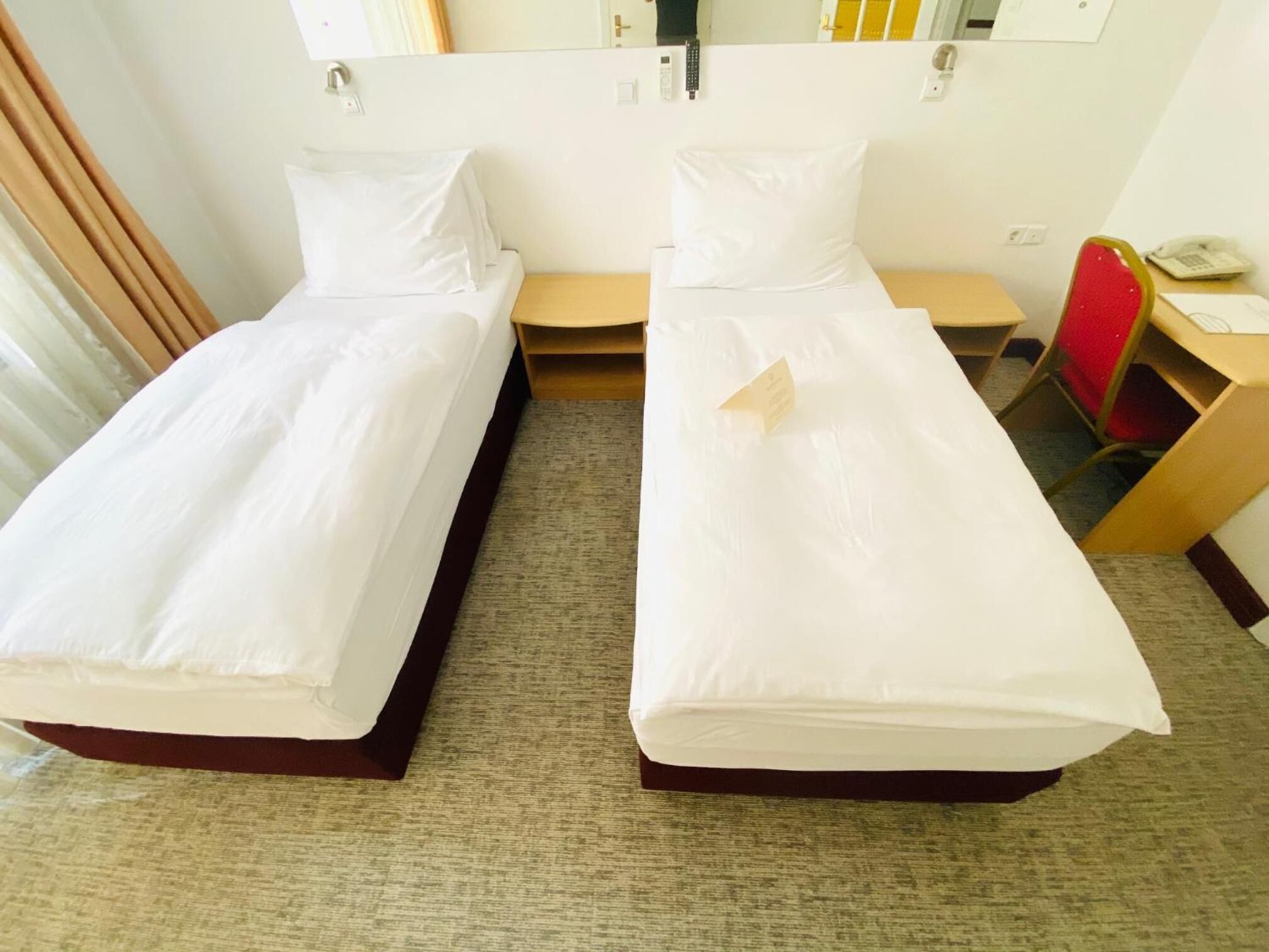 Two single beds with white linens, a wooden headboard, a small desk with a chair, and a mirror on the wall.