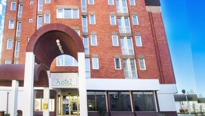 A multi-story hotel with a prominent archway entrance, a sign indicating it's a hotel, and a clear blue sky in the background. - Hotel Slavonija (Vinkovci)