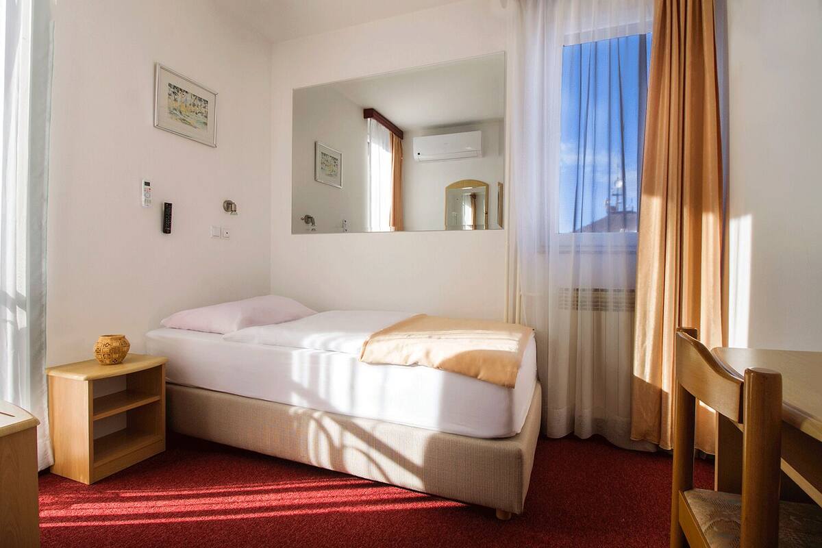 A hotel room with a bed, a bedside table, a mirror, and a window with curtains.