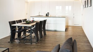 Eine moderne Küche mit weißen Schränken, einer zentralen Kochinsel und einem Essbereich mit Holztisch und schwarzen Stühlen.