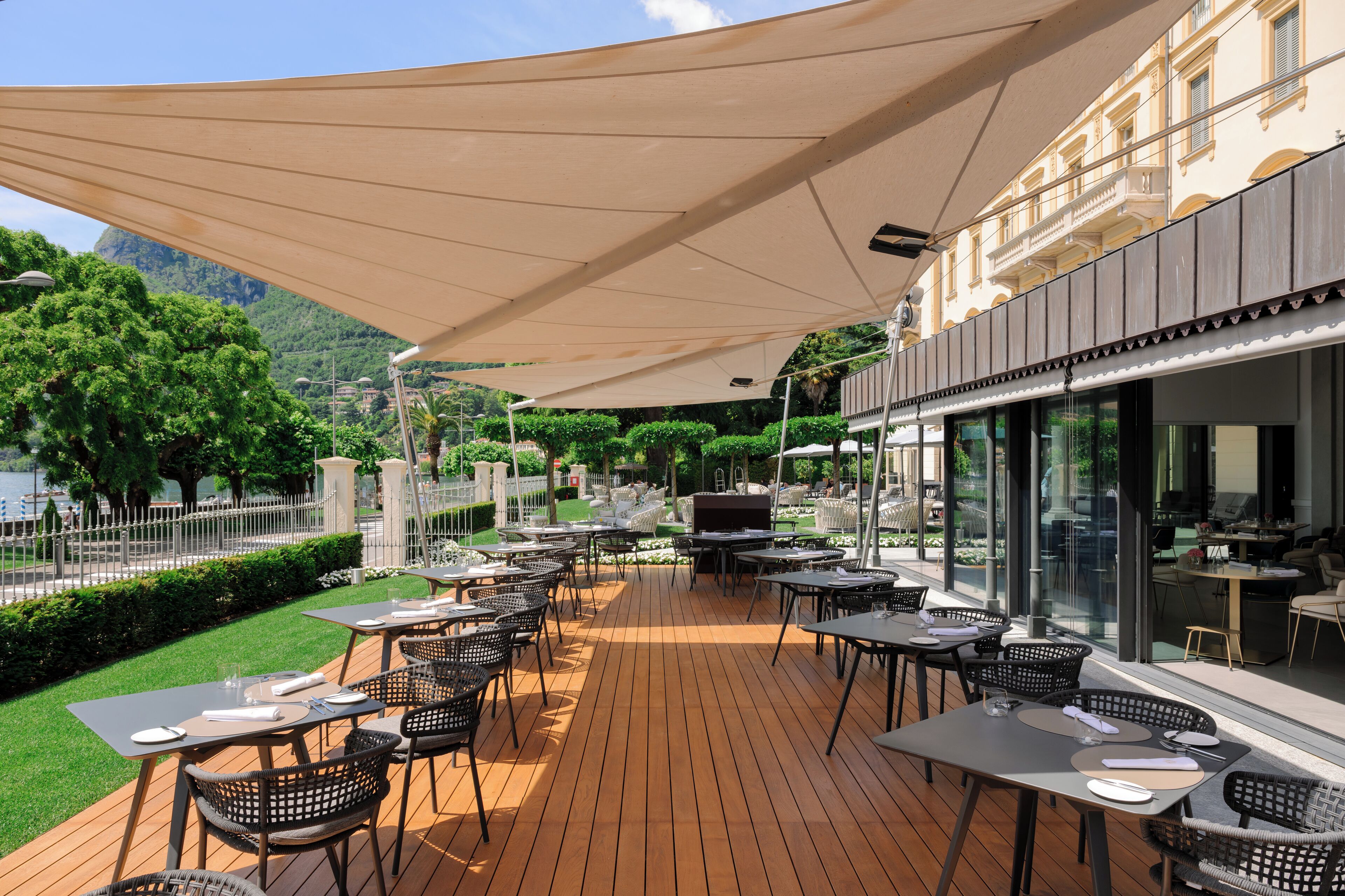 An outdoor patio with tables and chairs, a large canopy, and a view of a mountain and water.