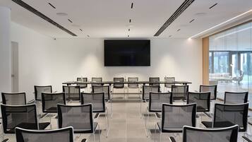 Una sala conferenze con un grande schermo piatto, diversi tavoli e sedie disposte per riunioni.