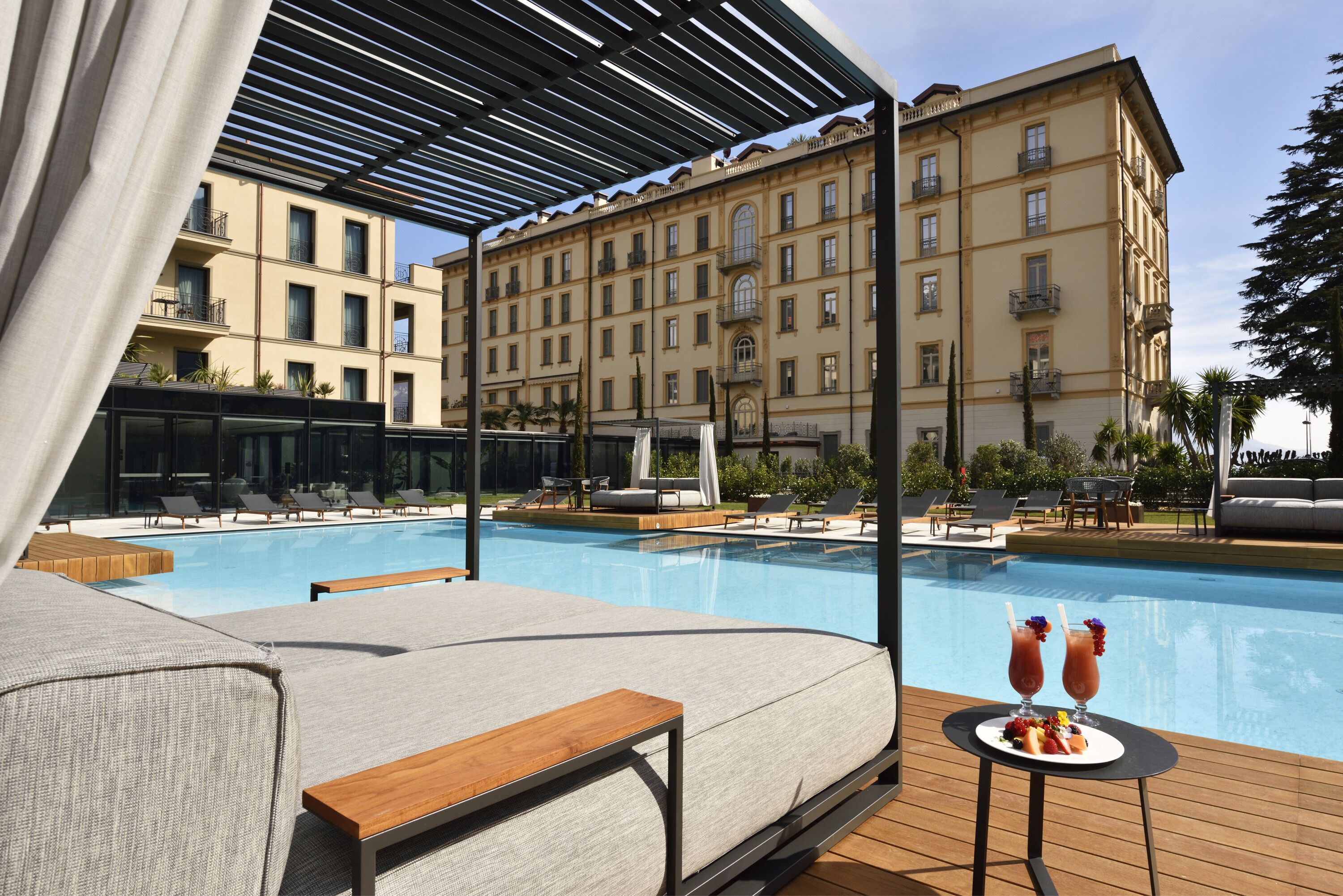 Area piscina con lettini, un tavolino con bevande e un edificio sullo sfondo.