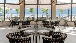 An outdoor dining area with tables and chairs, large windows, and a view of a lake and mountains. - Grand Hotel Victoria Concept & Spa, by R Collection Hotels (Menaggio)
