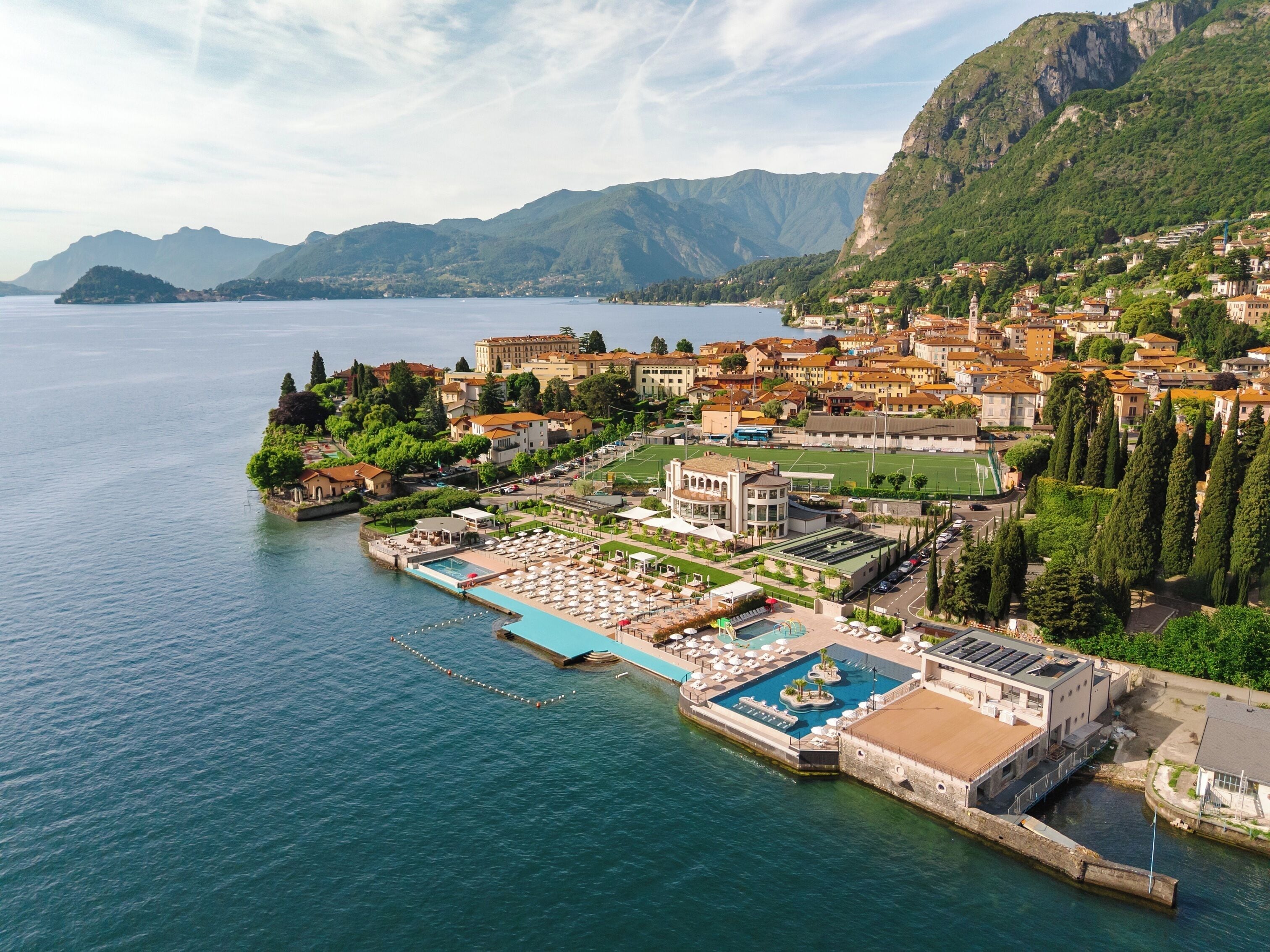 A coastal hotel with a swimming pool, a tennis court, and a view of the surrounding mountains.