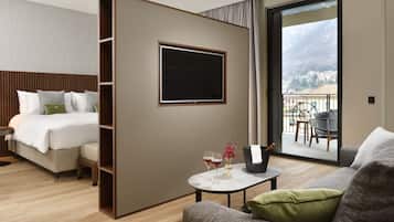 A modern hotel room with a bed, a small table with drinks, a sofa, a TV, and a balcony with a view of the mountains.