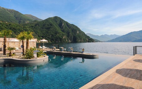 A pool area with lounge chairs and a view of a lake and mountains.