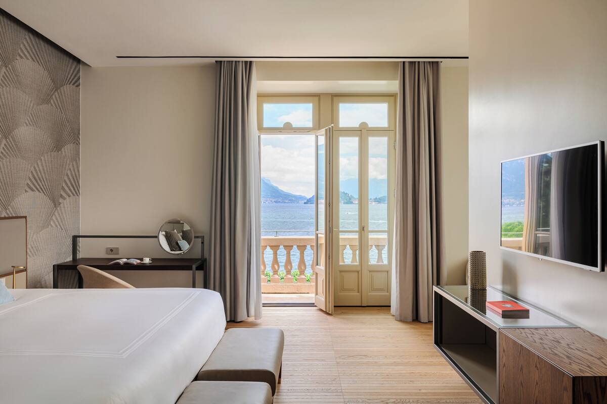 A hotel room with a bed, a desk, a TV, and a balcony with a view of the sea.