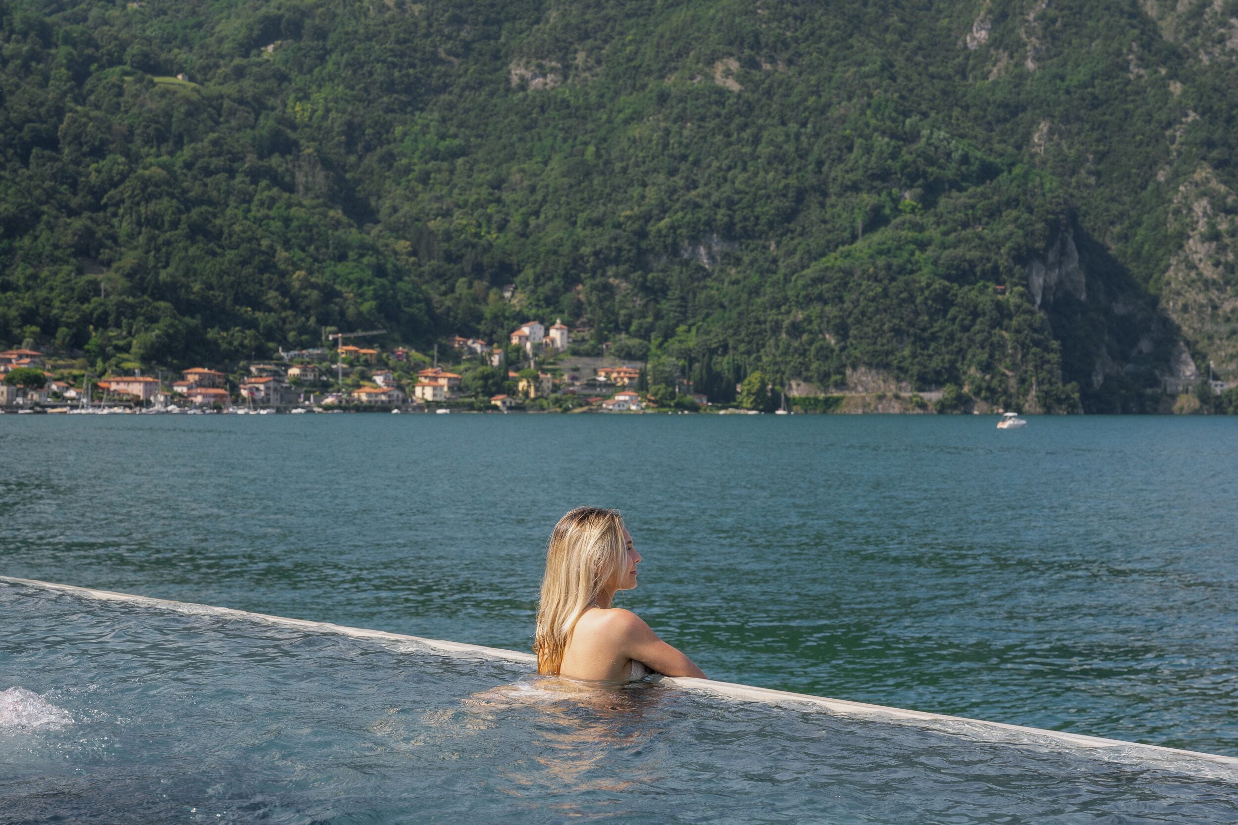 Uma pessoa em uma piscina com vista para um lago e casas ao fundo.
