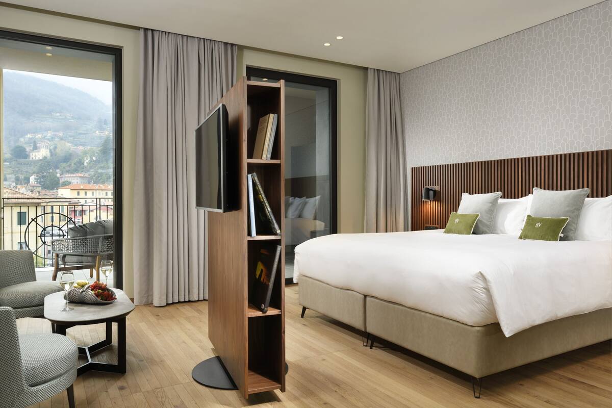 A hotel room with a large bed, a seating area with a table, and a bookshelf.