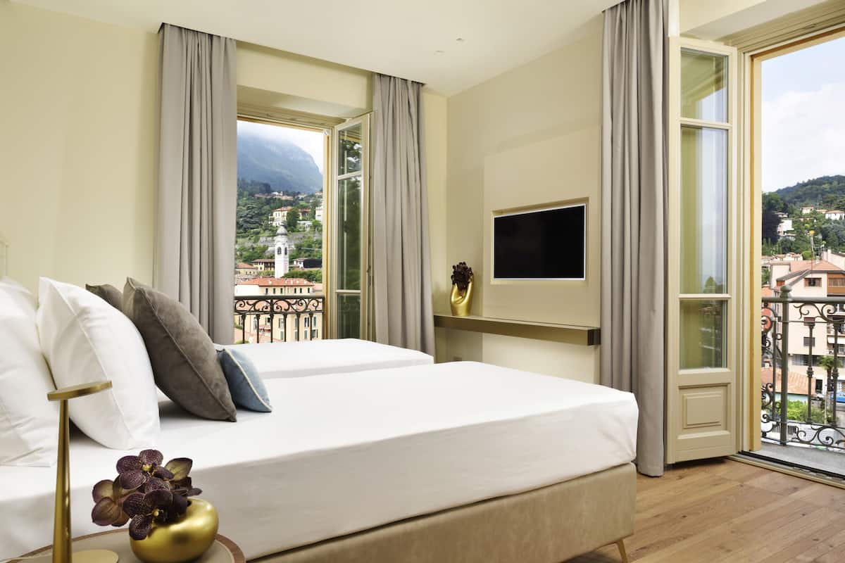 A hotel room with two beds, a TV, and a balcony with a city view.
