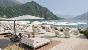 A beachside resort with sun loungers, umbrellas, and a wooden deck overlooking a lake with mountains in the background. - Grand Hotel Victoria Concept & Spa, by R Collection Hotels (Menaggio)