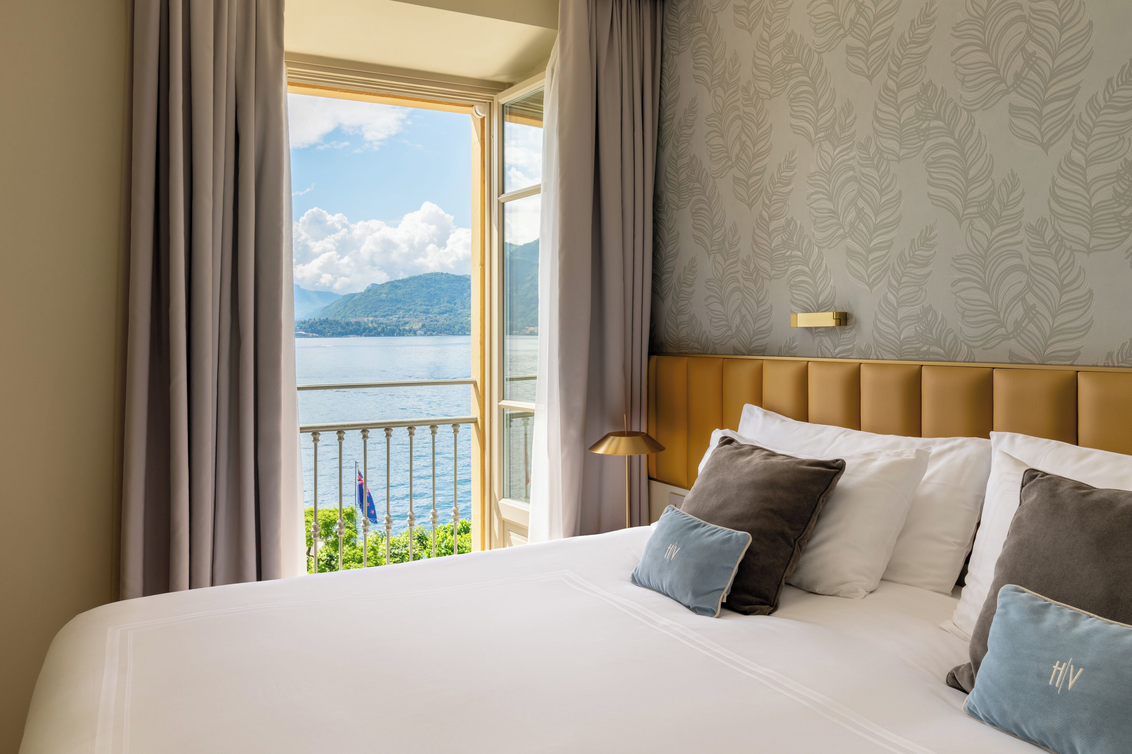 A hotel room with a large bed, a view of the sea, and a patterned wall.
