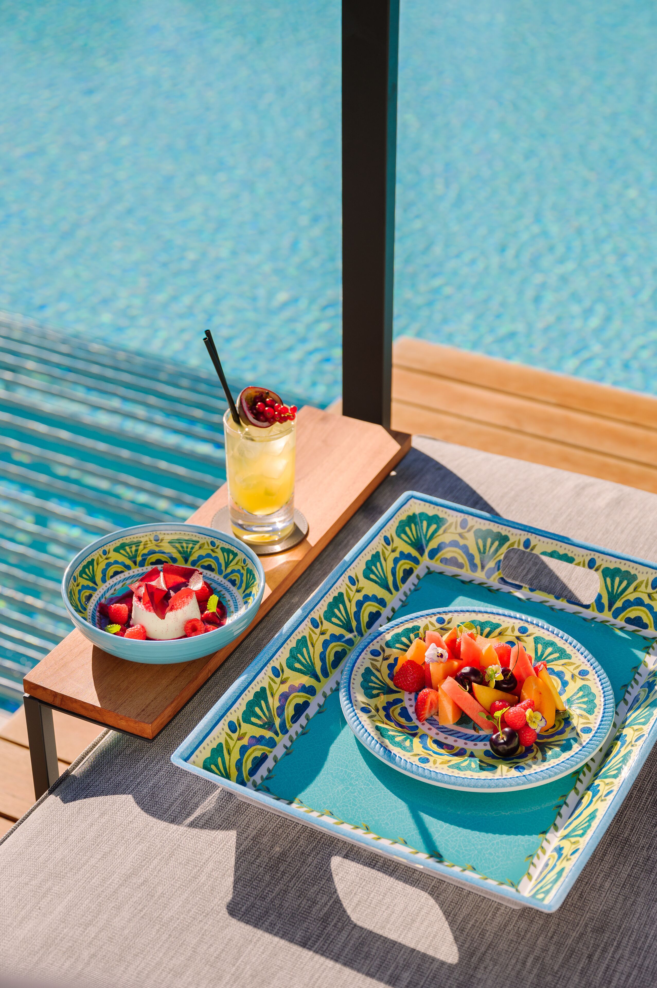 Mesa con frutero y bebida en una terraza junto a una piscina.