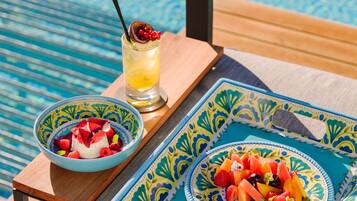 Mesa con frutero y bebida en una terraza junto a una piscina.