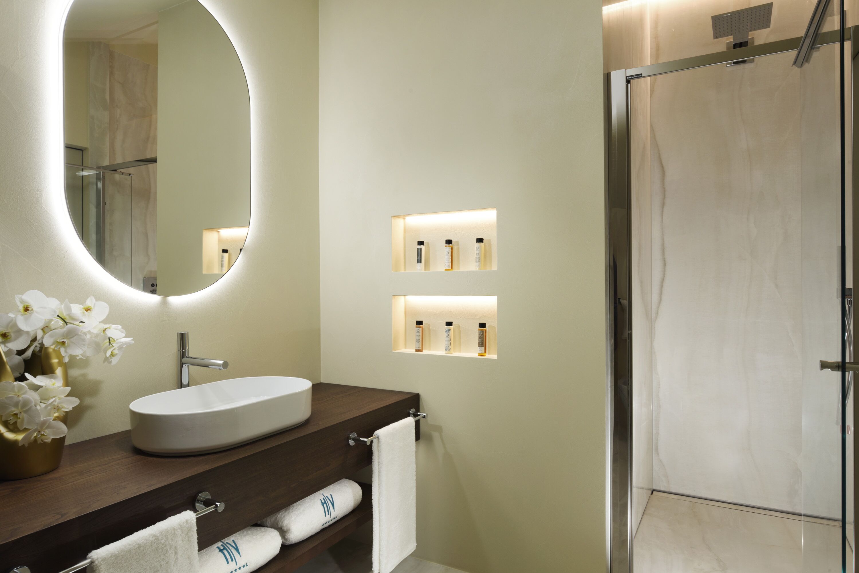 Une salle de bain moderne avec un miroir rond, un lavabo blanc et une douche à parois de verre.