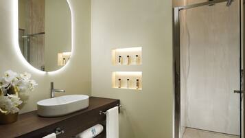 Une salle de bain moderne avec un miroir rond, un lavabo blanc et une douche à parois de verre.