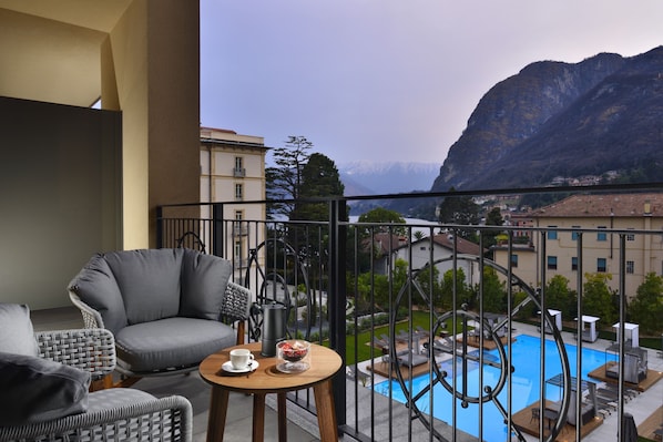 A balcony with a view of a mountain, a pool, and a dining area with chairs and a table. - Grand Hotel Victoria Concept & Spa, by R Collection Hotels (Menaggio)