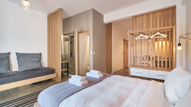 A modern bedroom with a bed, a seating area, a wooden wardrobe, and a shower area.