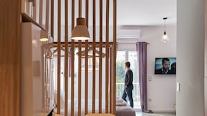 A modern living room with a wooden partition, a TV mounted on the wall, and a person walking in the background.