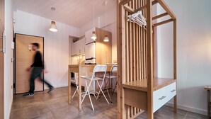 A modern kitchen with wooden cabinets, a dining table, and chairs. There is a person walking in the hallway.