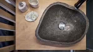 A stone sink with two cups and a bottle on a wooden surface.