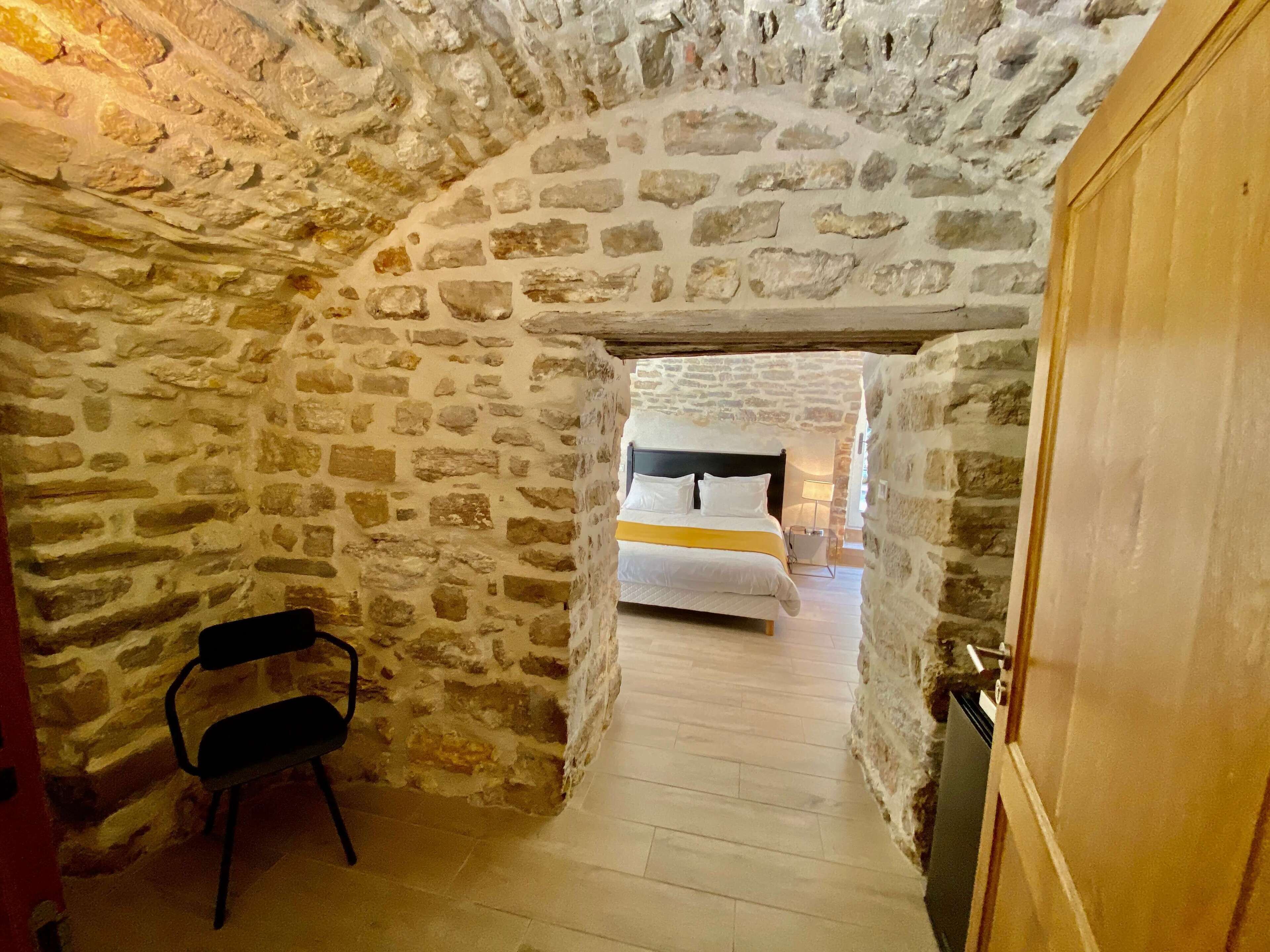 A narrow stone corridor leading to a bedroom with a bed and a bedside table.