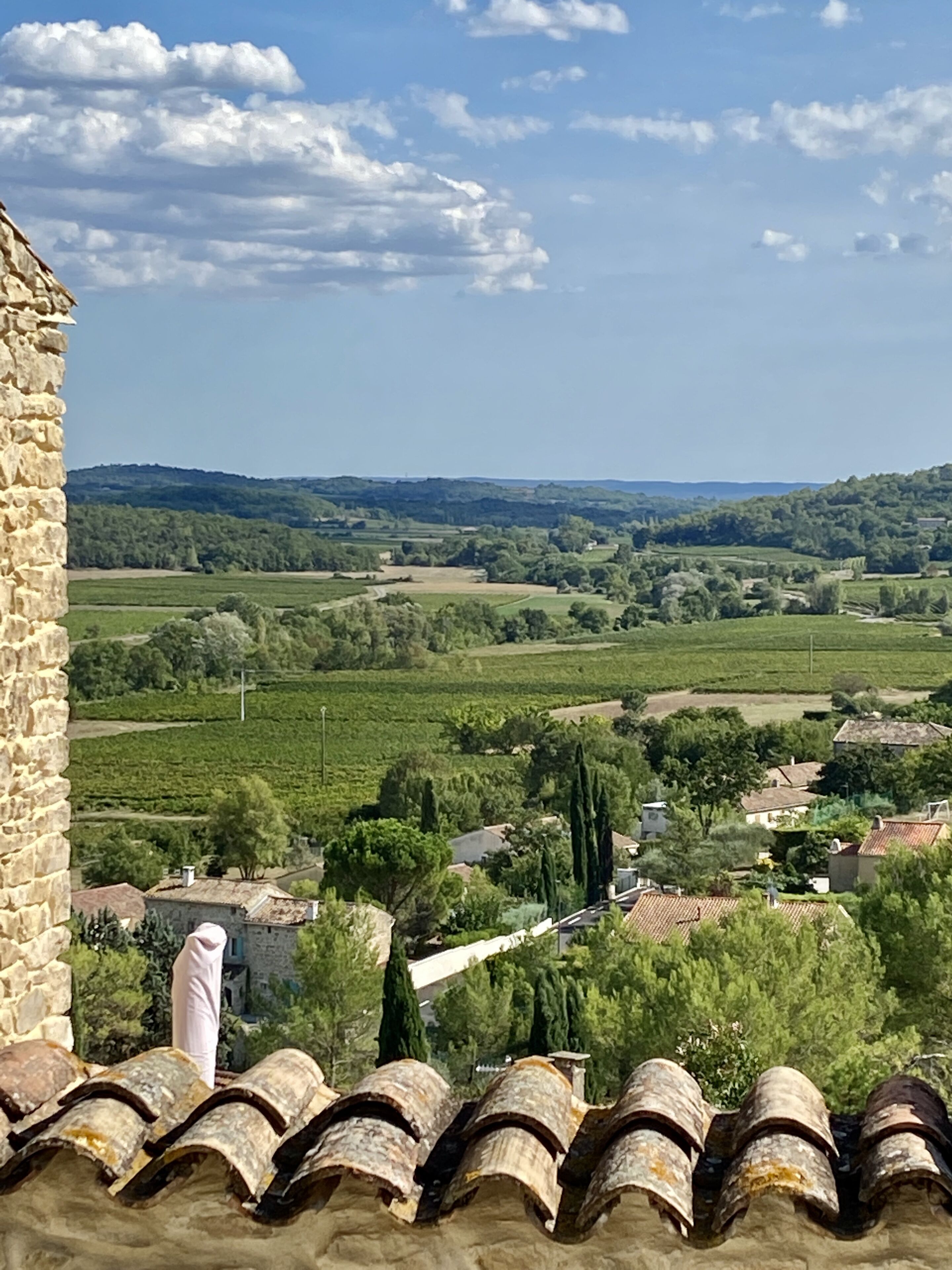 Ländliche Landschaft mit einem Steinhaus, Terrakotta-Dachziegeln und Blick auf grüne Felder und Bäume.